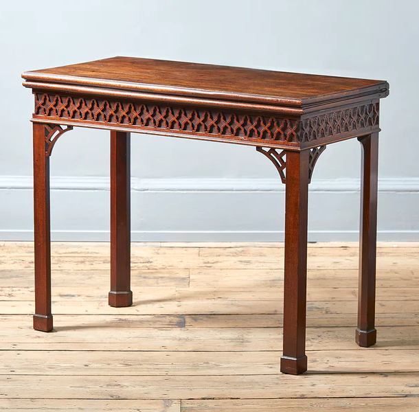 A George III mahogany folding card table, circa 1760. The moulded top opening to a baize lined interior, the blind fretwork deocrated frieze above square section legs surmunted by pierced brackets and on plinth feet, hinges stamped H Tibats
