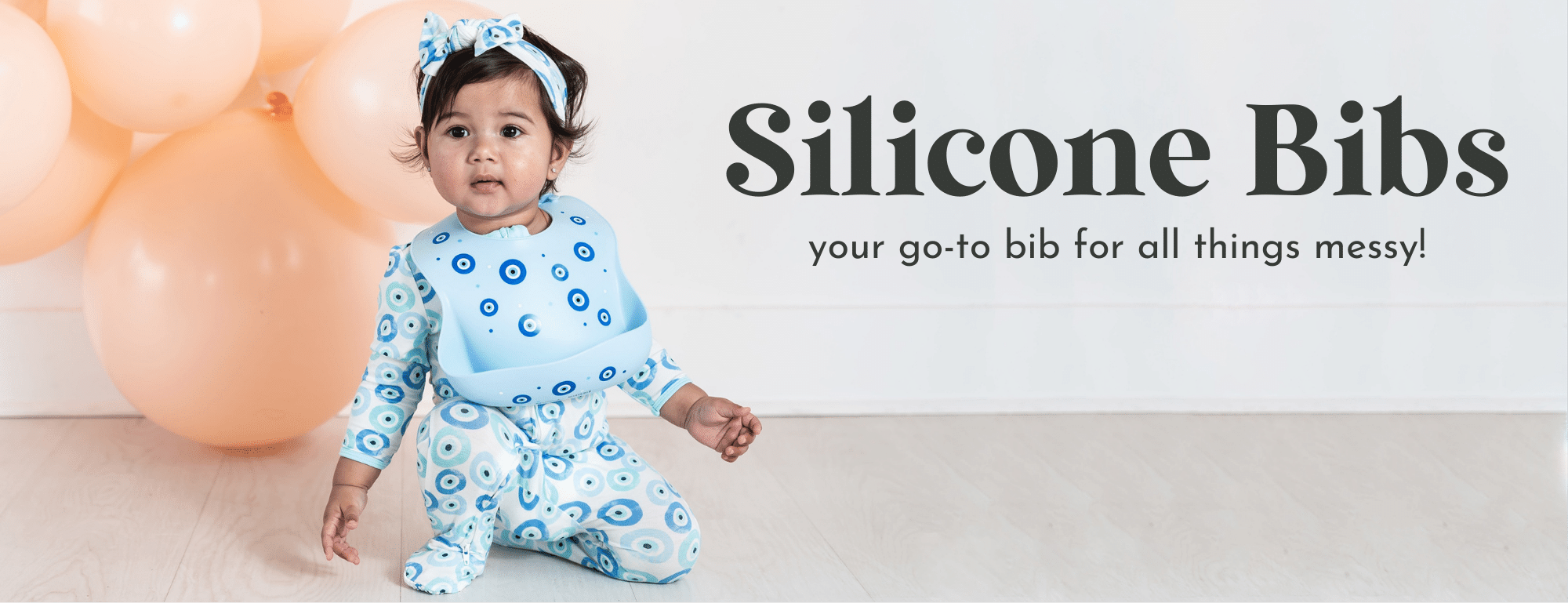 baby wearing evil eye silicone bib in front of peach balloons 